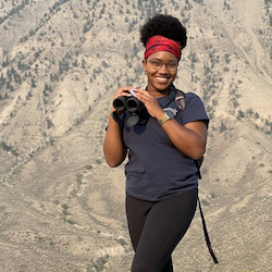 Sheridan Alford, smiling and holding binoculars in a mountainous setting.