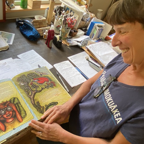 Artist Caren Loebel-Fried, smiling, looks at her work in a book. 