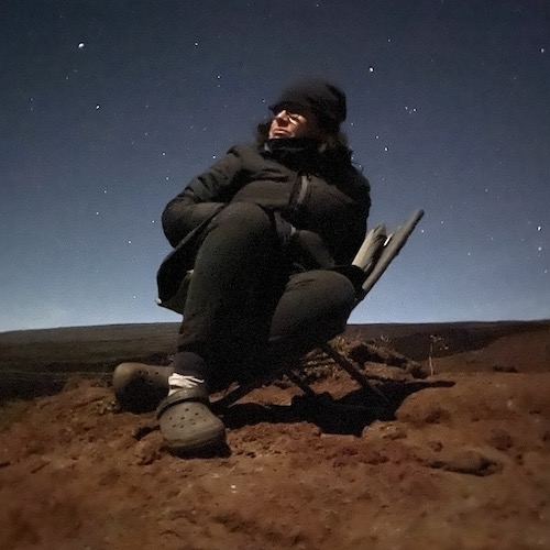 Charlotte Forbes Perry sits in a chair, bundled up, looking up to a starry night. 