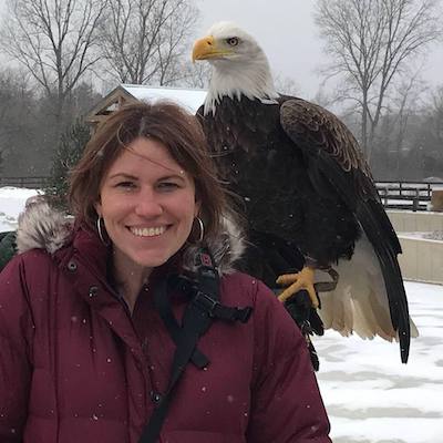 Photographer Jocelyn Anderson smiling in a snowy setting, with a Bald Eagle perched behind at shoulder level