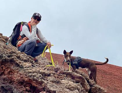 Wildlife biologist Michelle Reynolds sits on a slope of Mauna Loa, holding the yellow leash of her nearby "detector" dog, Slater.