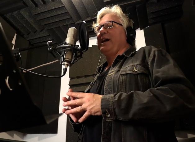BirdNote narrator Michael Stein speaks before a microphone in a recording studio.
