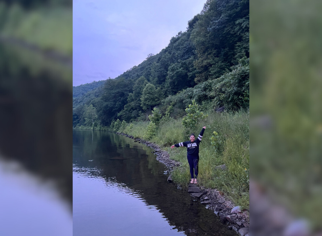 Woman wearing black stands on the edge of a lake, with arms stretched out