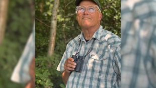 A photo of Jay Inslee with binoculars in a forest. 