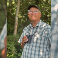 A photo of Jay Inslee with binoculars in a forest. 