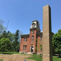 A brick custom-built Chimney Swift Tower stands in front of a historic schoolhouse that is now the home of public radio station WYSO in Yellow Springs, Ohio.