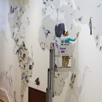 A photo of Jane Kim painting the Wall of Birds mural in a lift several feet off the ground.