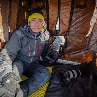 Photographer and author Noppadol Paothong, dressed for cold weather, sits inside a tent with openings for his cameras used for photographing wildlife.